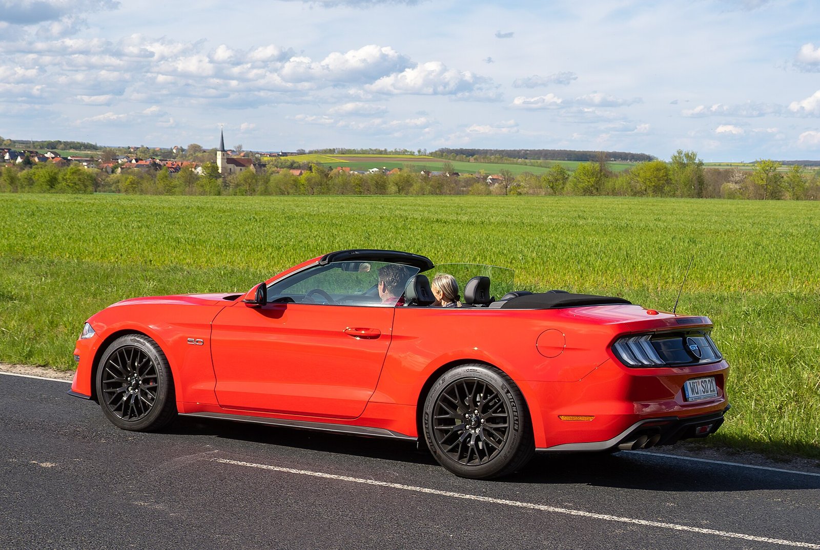 Красный кабриолет Ford Mustang с опущенной крышей на фоне поля